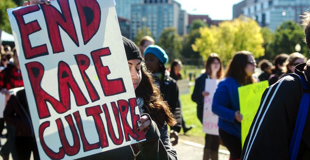 Image of people walking holding signs, one of which reads "End Rape Culture".