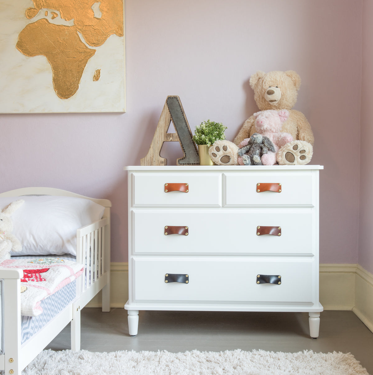 A white chest of drawers in a white and lilac baby nursery with three colors of leather Morrison bin pull handles, in Honey, Dark Brown, and Black