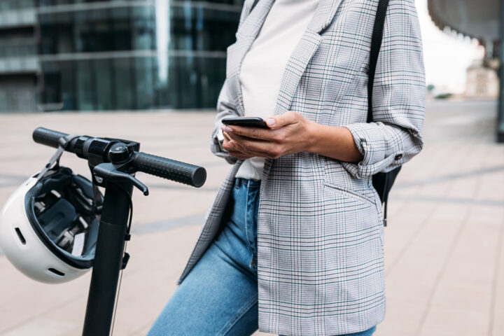 Frau, die eine App auf einem Mobiltelefon verwendet, um einen Elektroroller zu entriegeln.