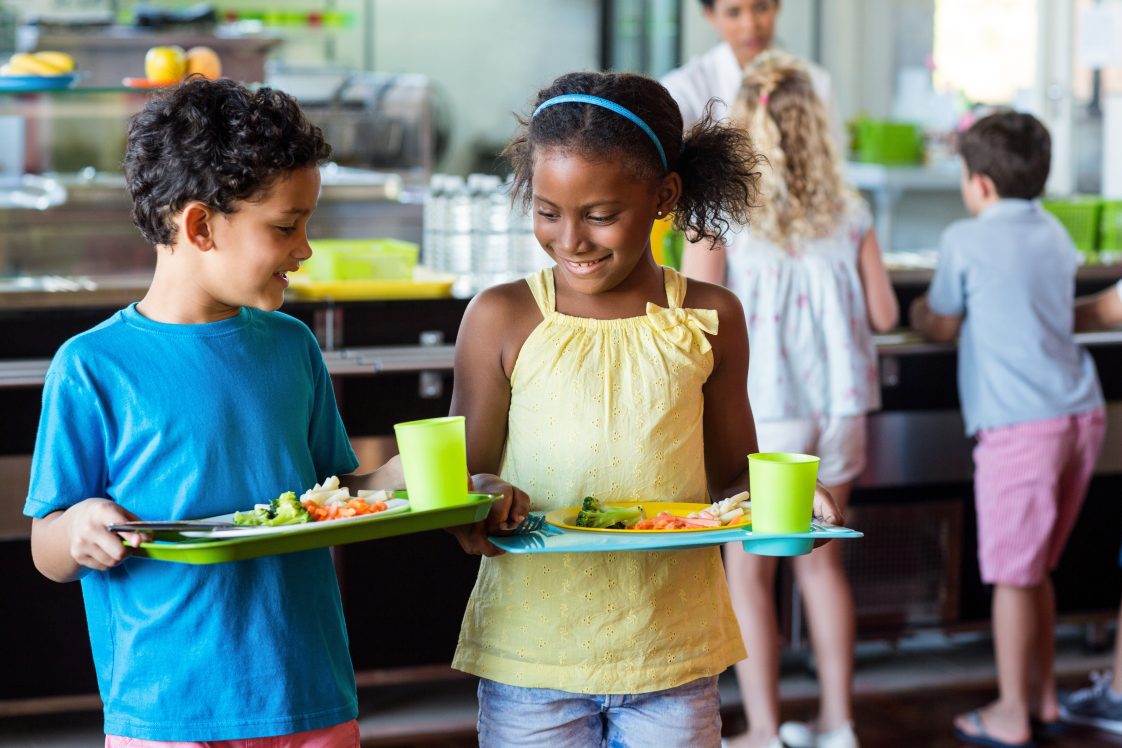 School children holding food tray in a cafeteria.