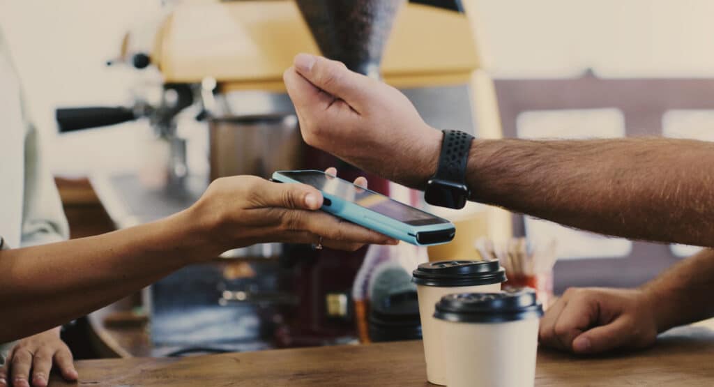 Person paying at a cafe with smartwatch held over mobile checkout device