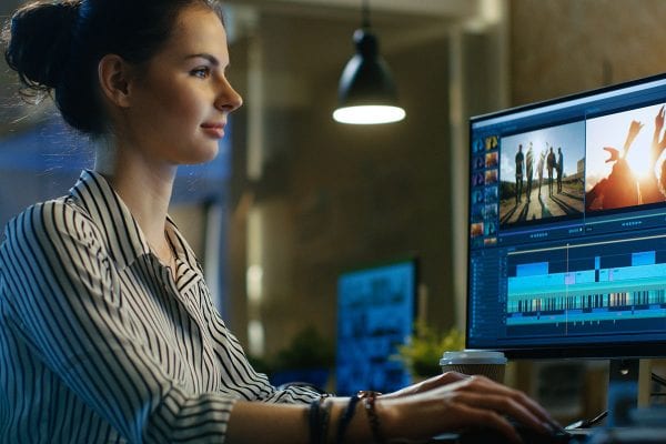 Young female video editor works with footage on her desktop computer in a creative studio.