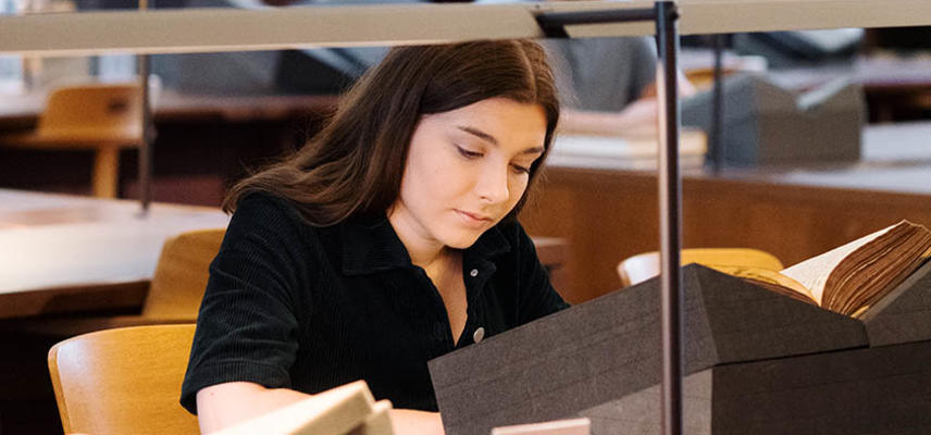 A woman with dark hair sits at a table, using a book on a book rest