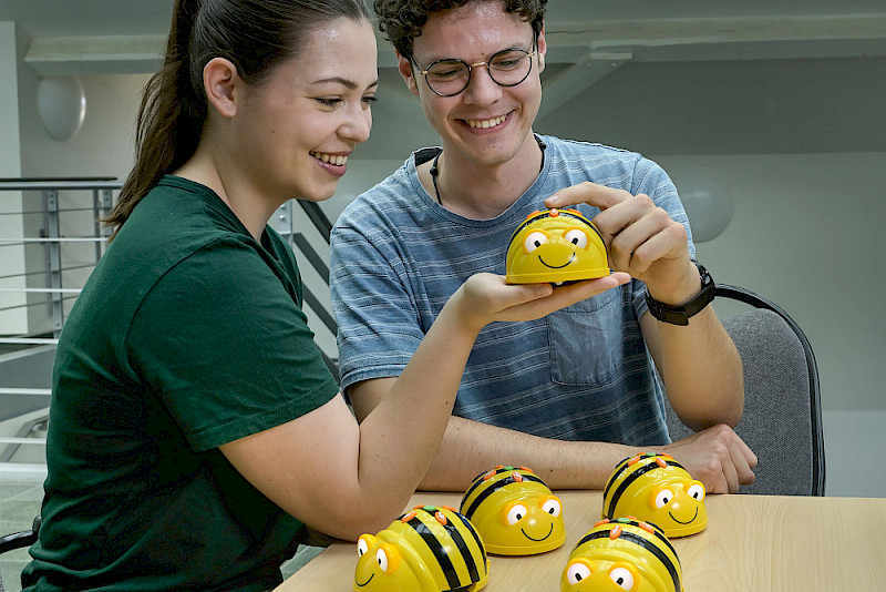 Die Lehramtsstudierenden Corinna Döhner und Simon Herbrich schauen sich Bee-Bots an, mit denen Schülerinnen und Schülern im Mathematikunterricht die Grundlagen von Algorithmen erklärt werden können.