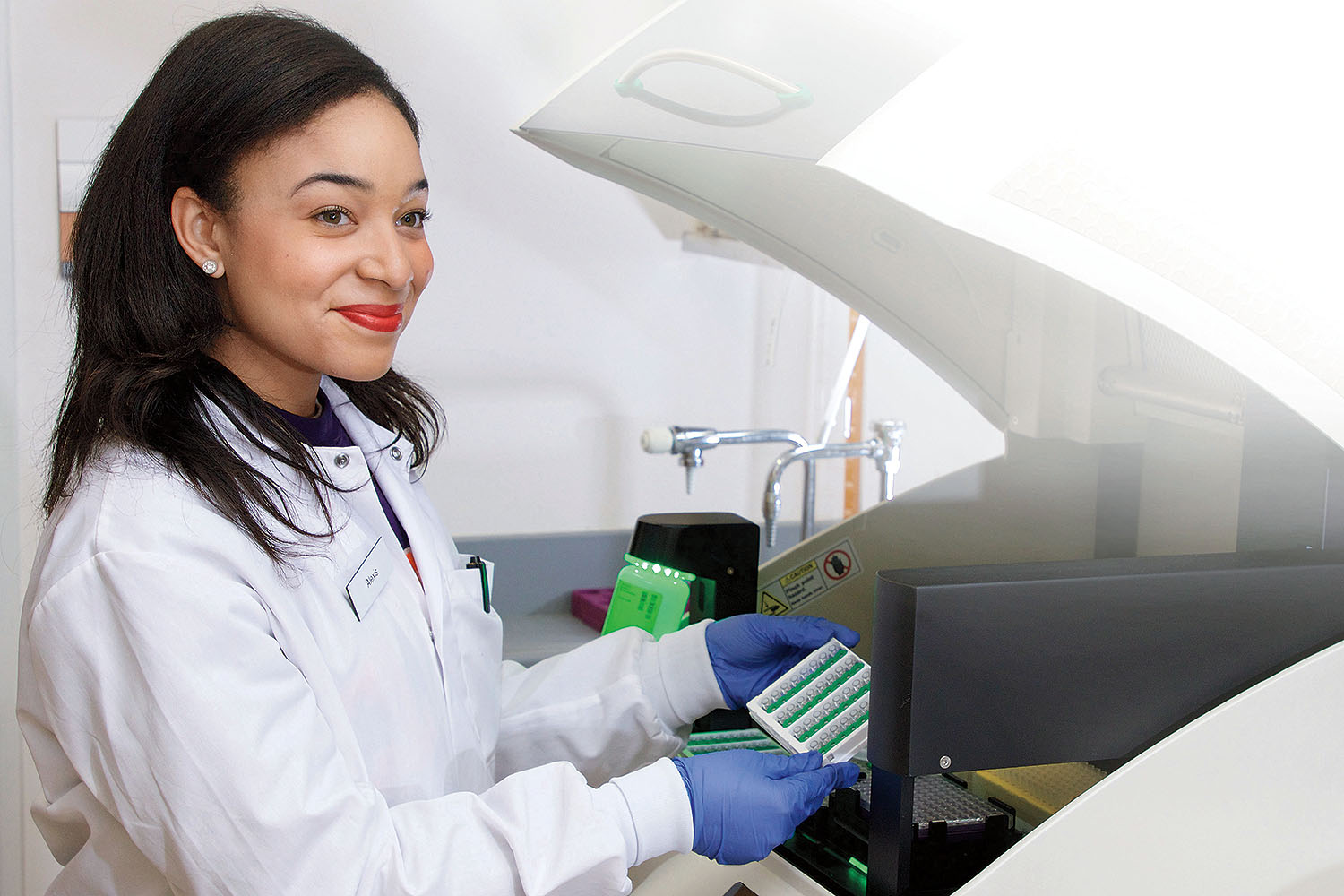 Female student holding green tray of vials, in front of diagnostic machine.