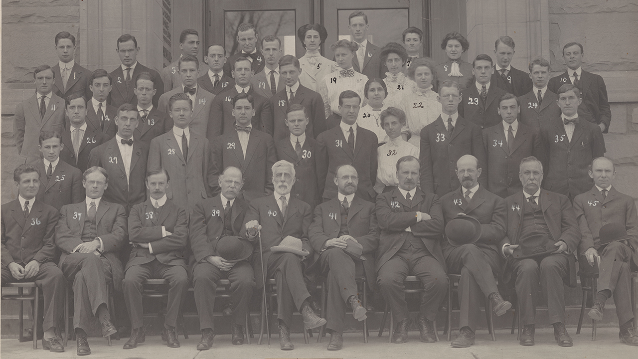 37 men and 8 women pose in front of a building.