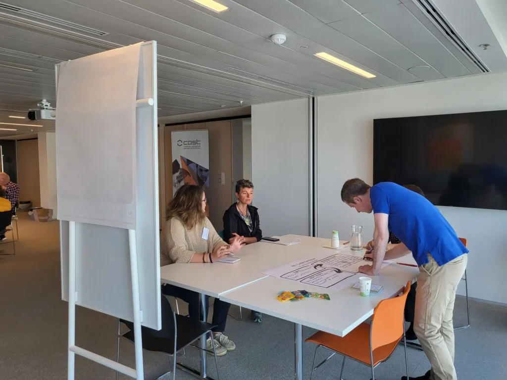 Three people working at a table writing notes with a white board to the side