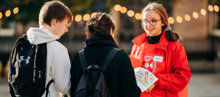 ambassador in red jacket talks to two potential students