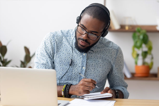 Man sat down working in office writing on pad