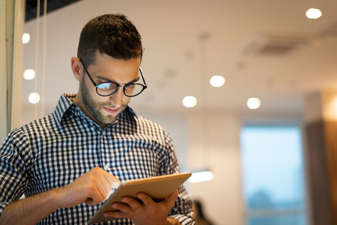 Man stood in office looking at tablet