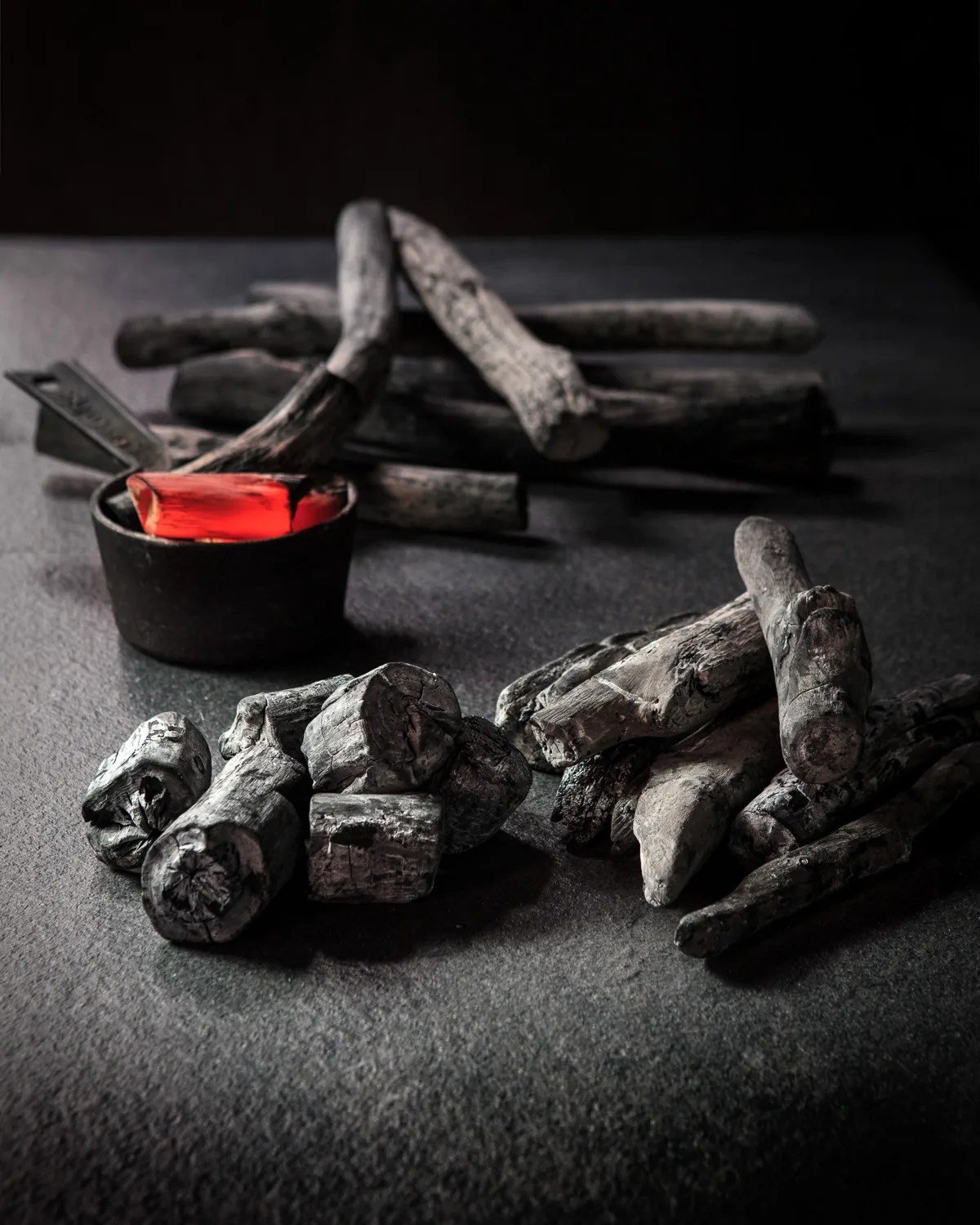 Image of bichotan charcoal logs sitting on grey surface. One is heated up red.