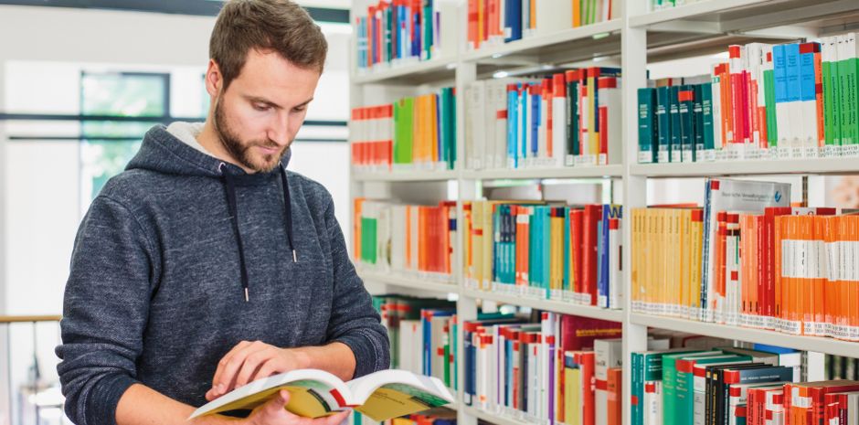 Studierender des Fachbereichs Verwaltungswissenschaften in der Bibliothek des Fachbereichs mit Fachliteratur.