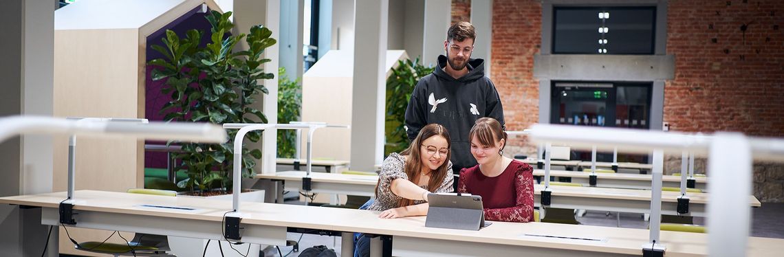 Drei Studierende der Verwaltungsökonomie schauen in der Bibliothek der Hochschule Harz auf ein Tablet.