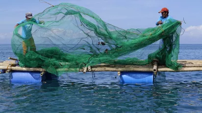 Fishers folding a green fishing net next on a handmade boat