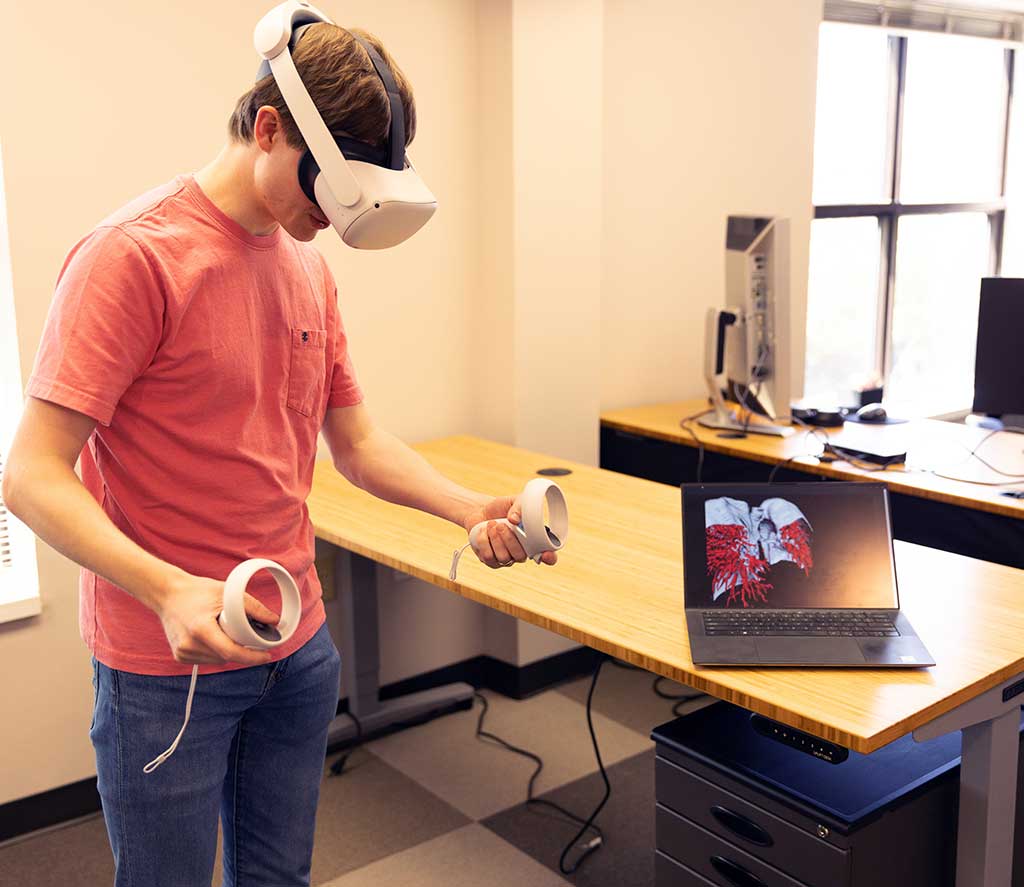 Person demonstrating Virtual Reality goggles with laptop showing internal of human body.