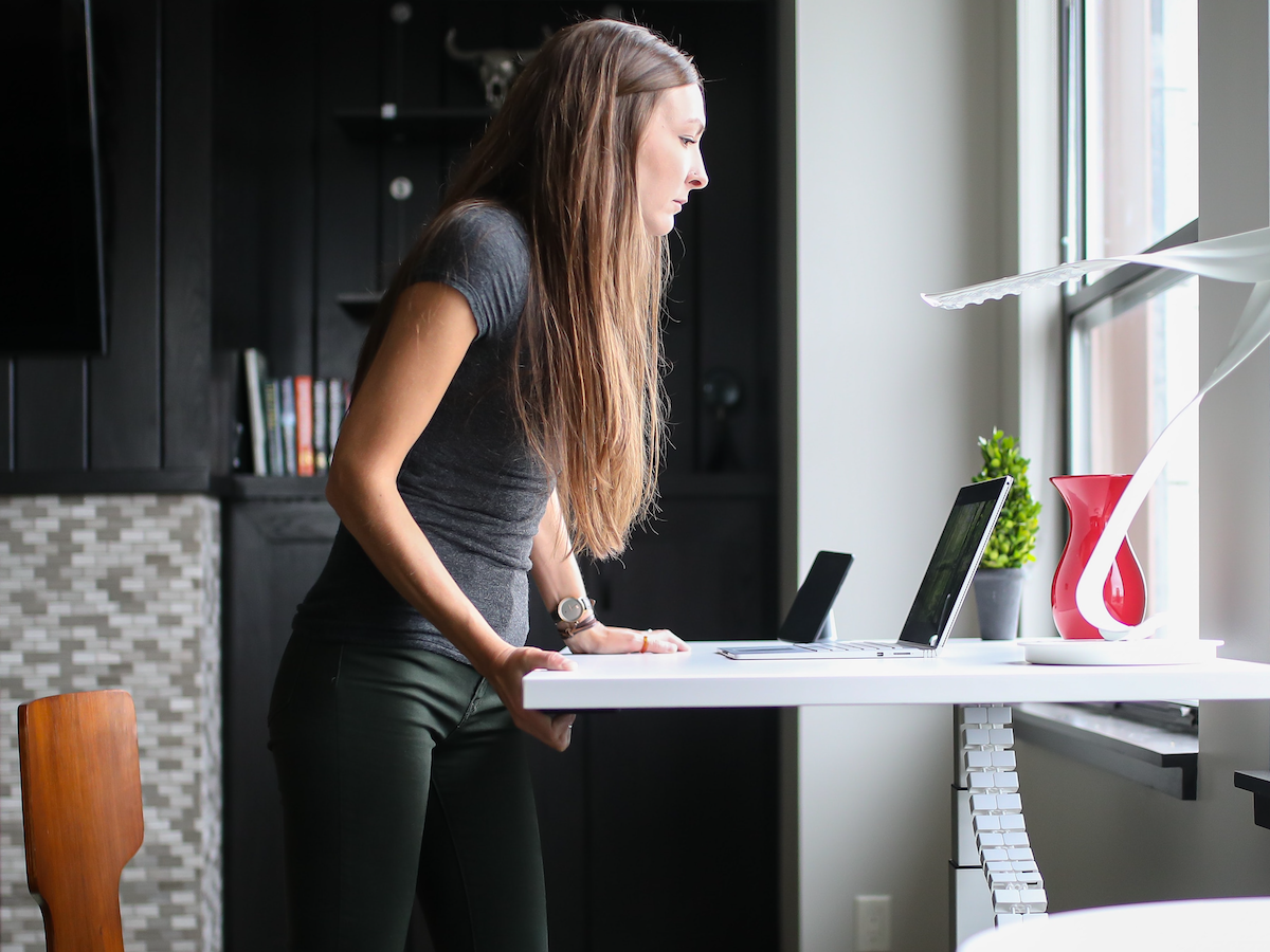 a white women pressing a button on a standing desk to move it up