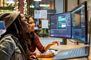 Two women in an office looking at a computer screen together and smiling.