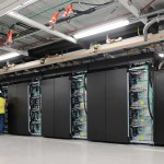 Two people stand in front of a tall row of computing stacks