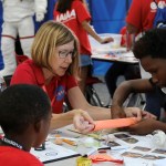 An adult sitting at a table with students doing an activity