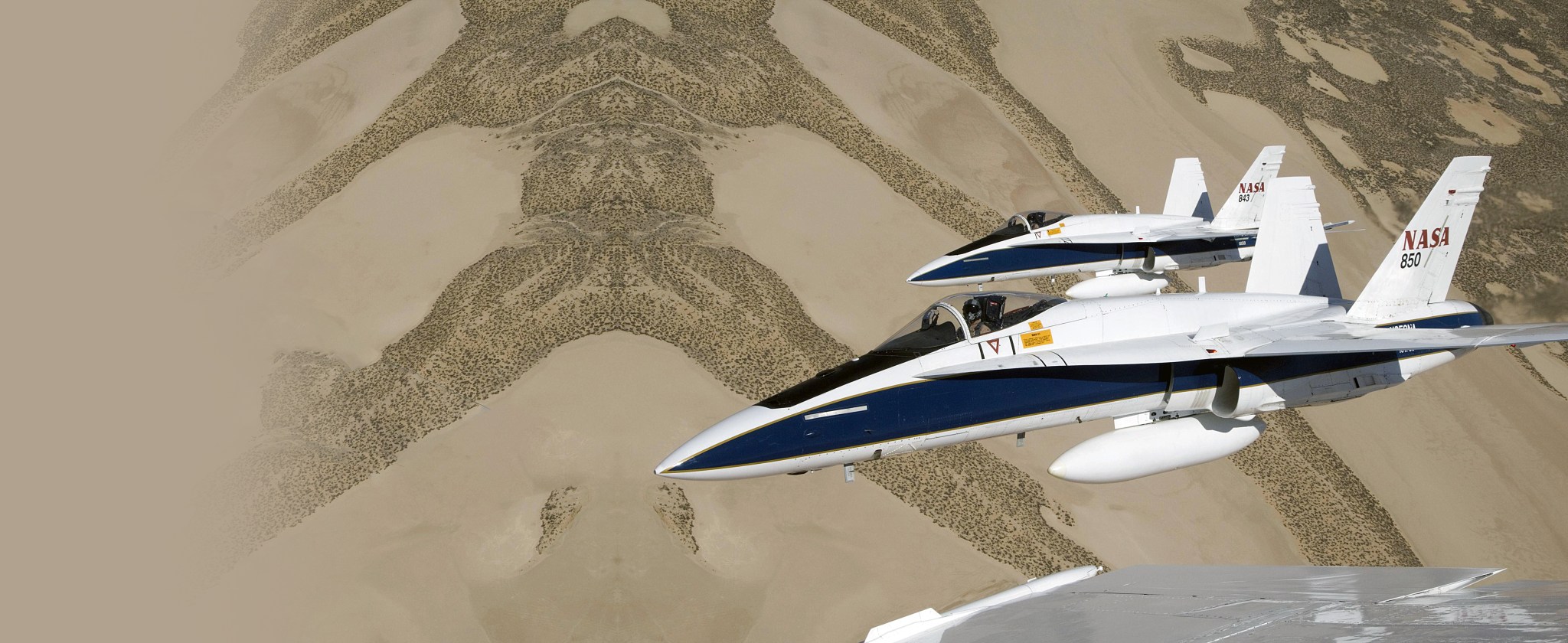 Two fighter jets now used by NASA for research are seen above the desert from the cockpit window of a third jet.