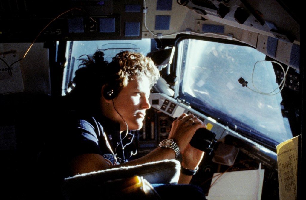 Astronaut Kathryn D. Sullivan, 41-G mission specialist, uses binoculars for a magnified viewing of earth through the forward cabin windows.