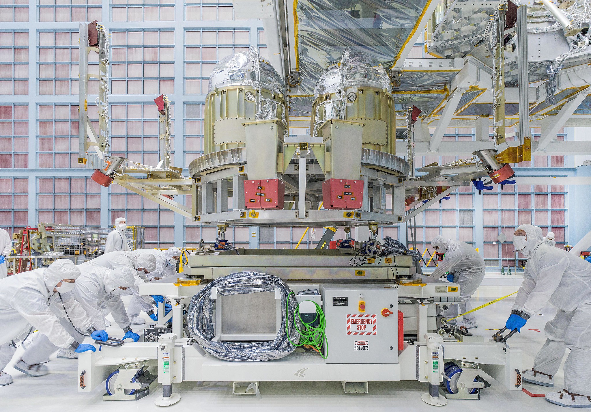 people in white, full-body "bunny suits" position hardware in a gleaming metallic clean room at NASA Goddard