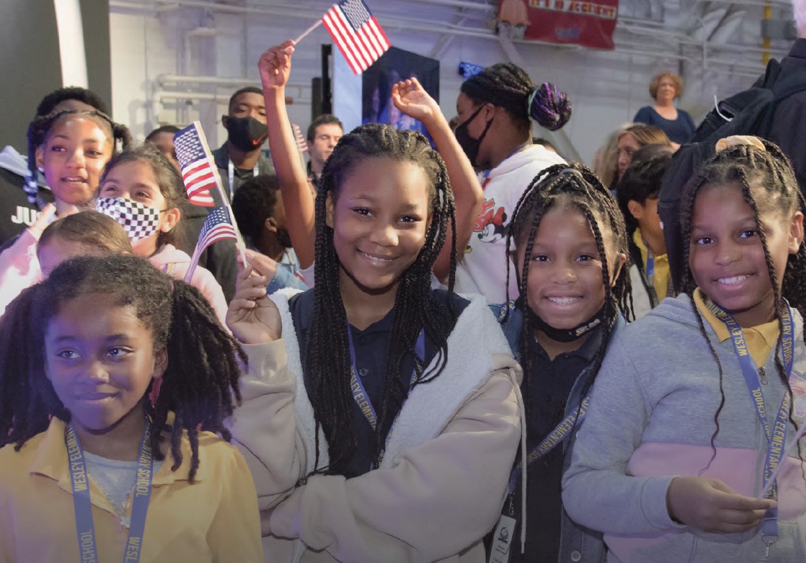 Students holding flags pose inside hanger