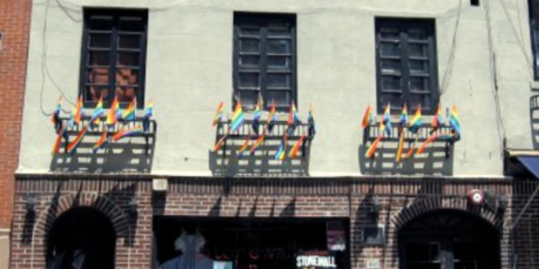 Image of the buildings that made up the original Stonewall Inn at 51-53 Christopher Street in Greenwich Village in New York City. Pride flags fly outside the windows on the second floor.
