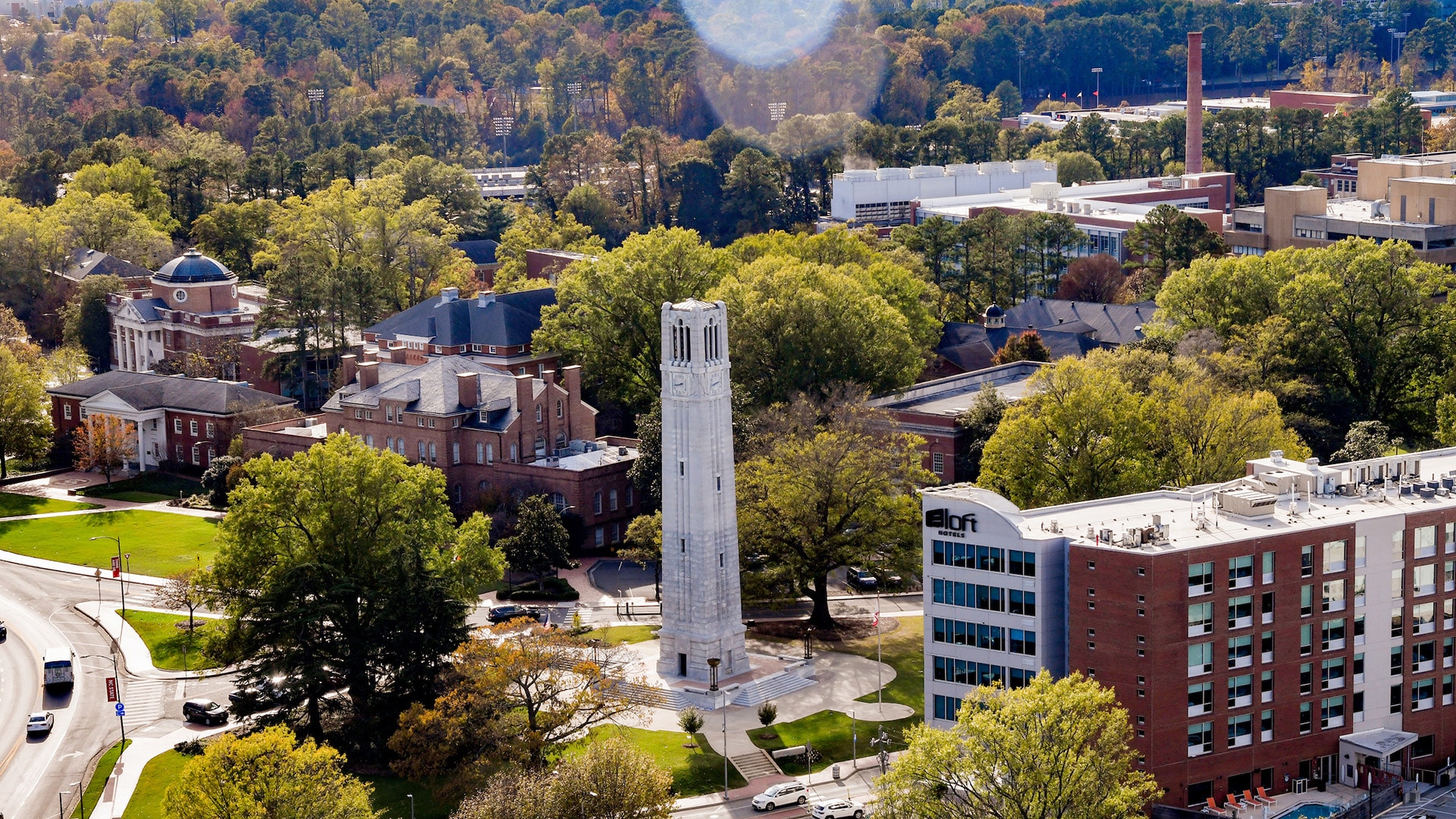 An aerial view of NC State's campus, showing the Belltower, Holladay Hall and the State College smokestack.