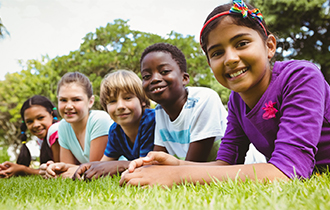 Group of happy children laying in grass outside.