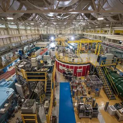 View from near ceiling shows NCNR guide hall filled with big pieces of scientific equipment, including several long cylindrical "guides" running toward the far end of the room. 