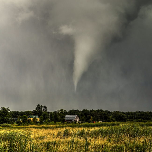 A storm with a condensed funnel cloud that is not touching the ground. The funnel cloud appears to be poised over a rural home.