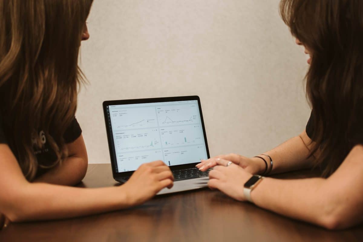 Two people sat around a desk looking at a reporting tool displayed on a laptop