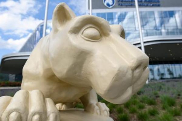 A close-up of a Nittany Lion statue with Hampden Medical Center in the background, slightly out of focus.