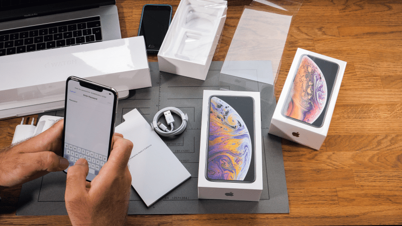 A person taking a new iPhone out of a box on a wooden table.