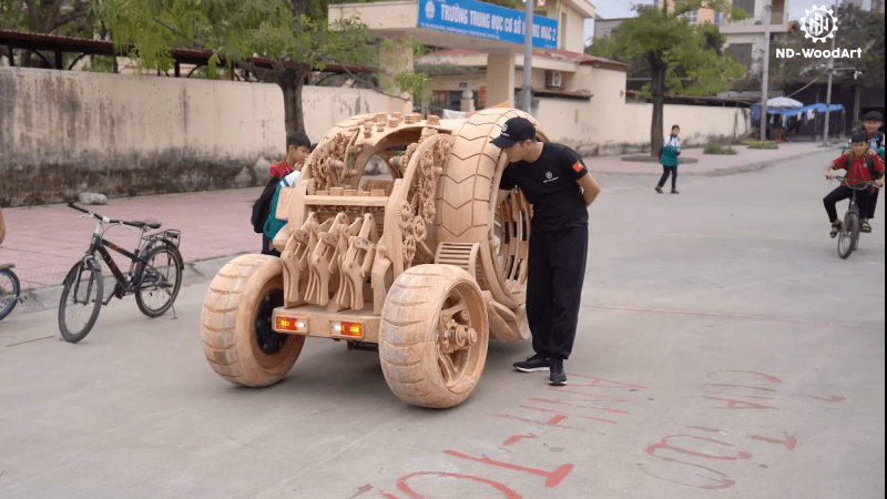 Futuristic wooden children's car with creator standing next to it.