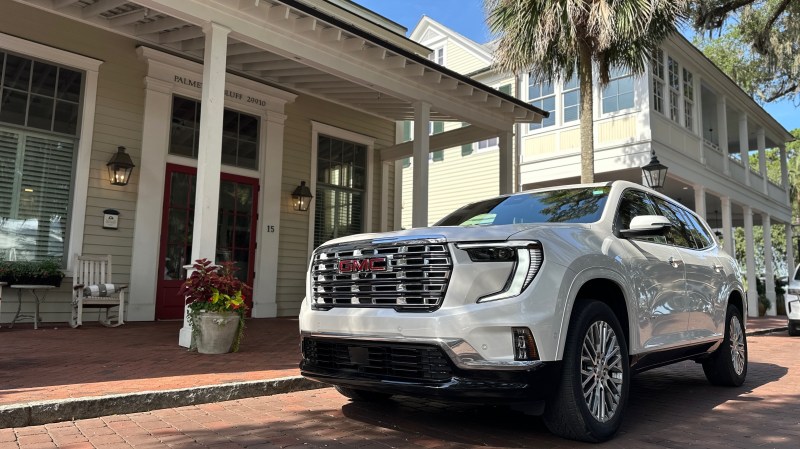 a large SUV parked in front of a colonial-style building. palm trees in the background