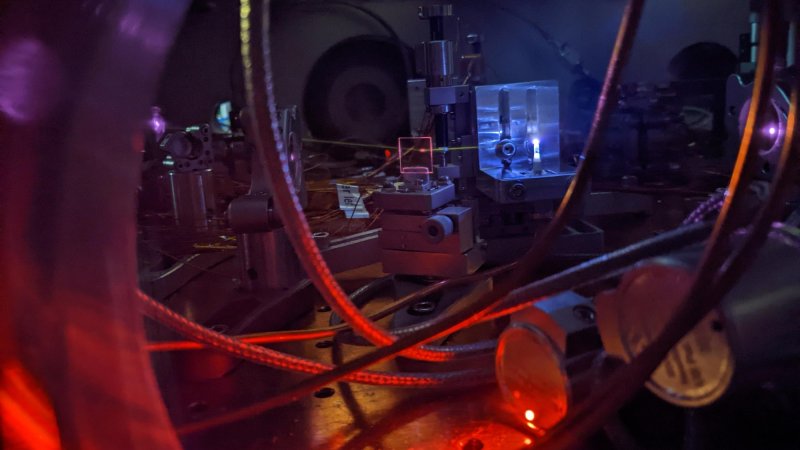 A powerful laser shines into a jet of gas, creating a bright plasma and generating ultraviolet light. The light leaves a visible white line as it interacts with leftover gas in the vacuum chamber. This process helps scientists precisely measure the energy needed to excite the thorium-229 nucleus, which is the core of a future nuclear clock.