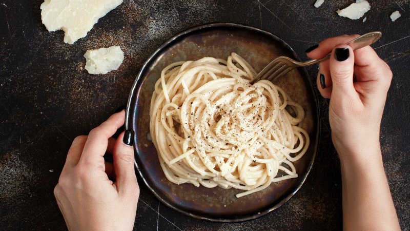 Woman's hands using fork to stir bowl of pasta