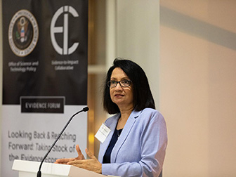 Penn State President Neeli Bendapudi speaks at a podium in front of a banner displaying the White House Office of Science and Technology Policy and Penn State's Evidence-to-Impact Collaborative