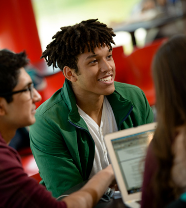 A student smiles as he works with a small group around a round table in the Student Activities Center