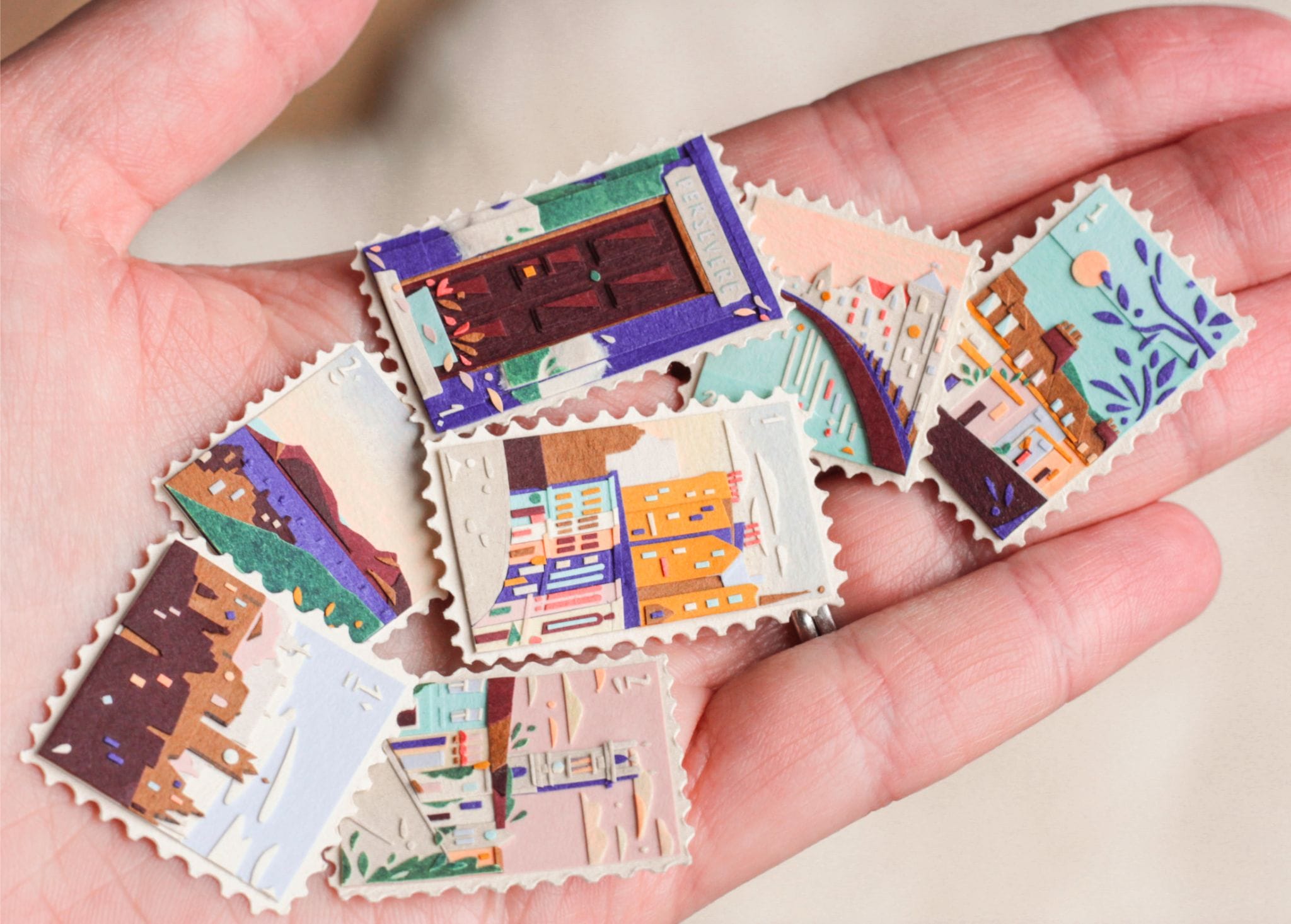 a hand holds up a collection of small, vibrant collages, each shaped like a stamp. they depict scenes with a building, water, architecture, and patterned designs