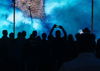 A group of people viewing and taking photographs of an art display with a blue background and a pink design.