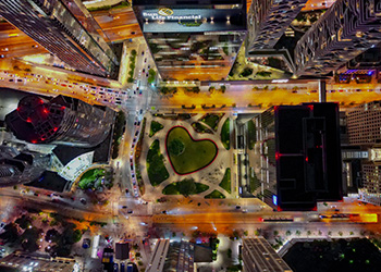 A bird's eye view at night time of a heart shaped pond between lit up skyscrapers.