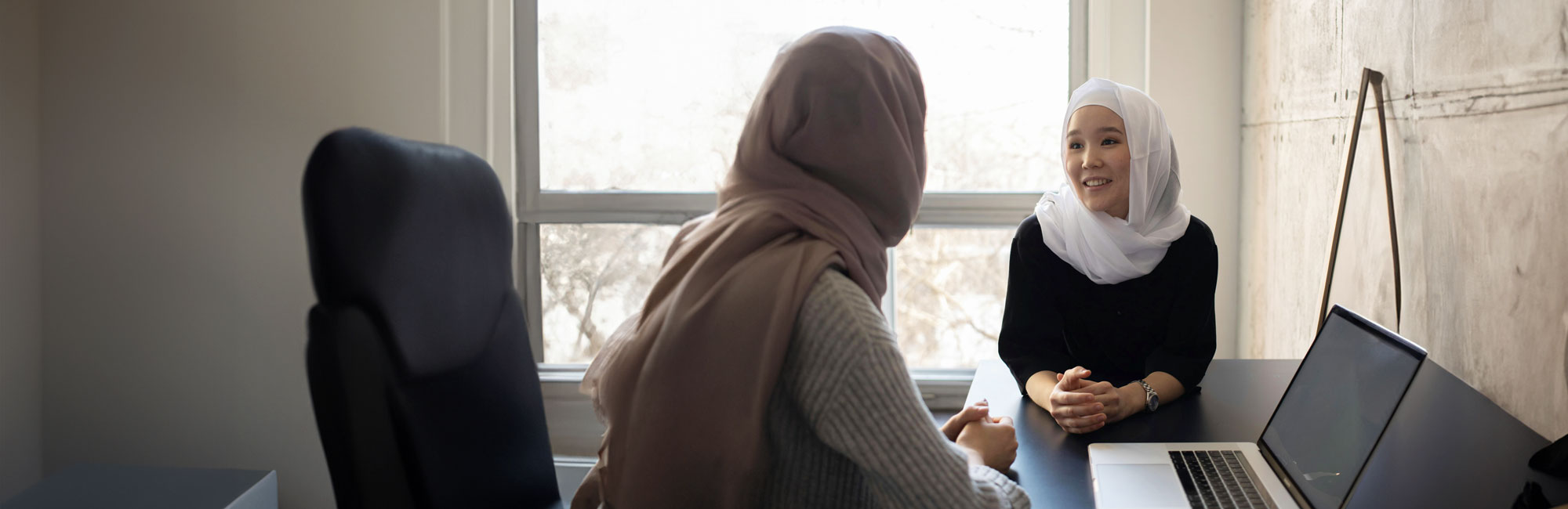 Muslim woman wearing a hijab in conversation with a colleague.