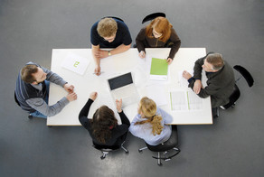 Von oben fotografiert: Sechs Personen sitzen mit ihren Laptops um einen weißen Tisch herum