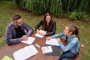 Studierende sitzen um einen Tisch im freien und arbeiten.