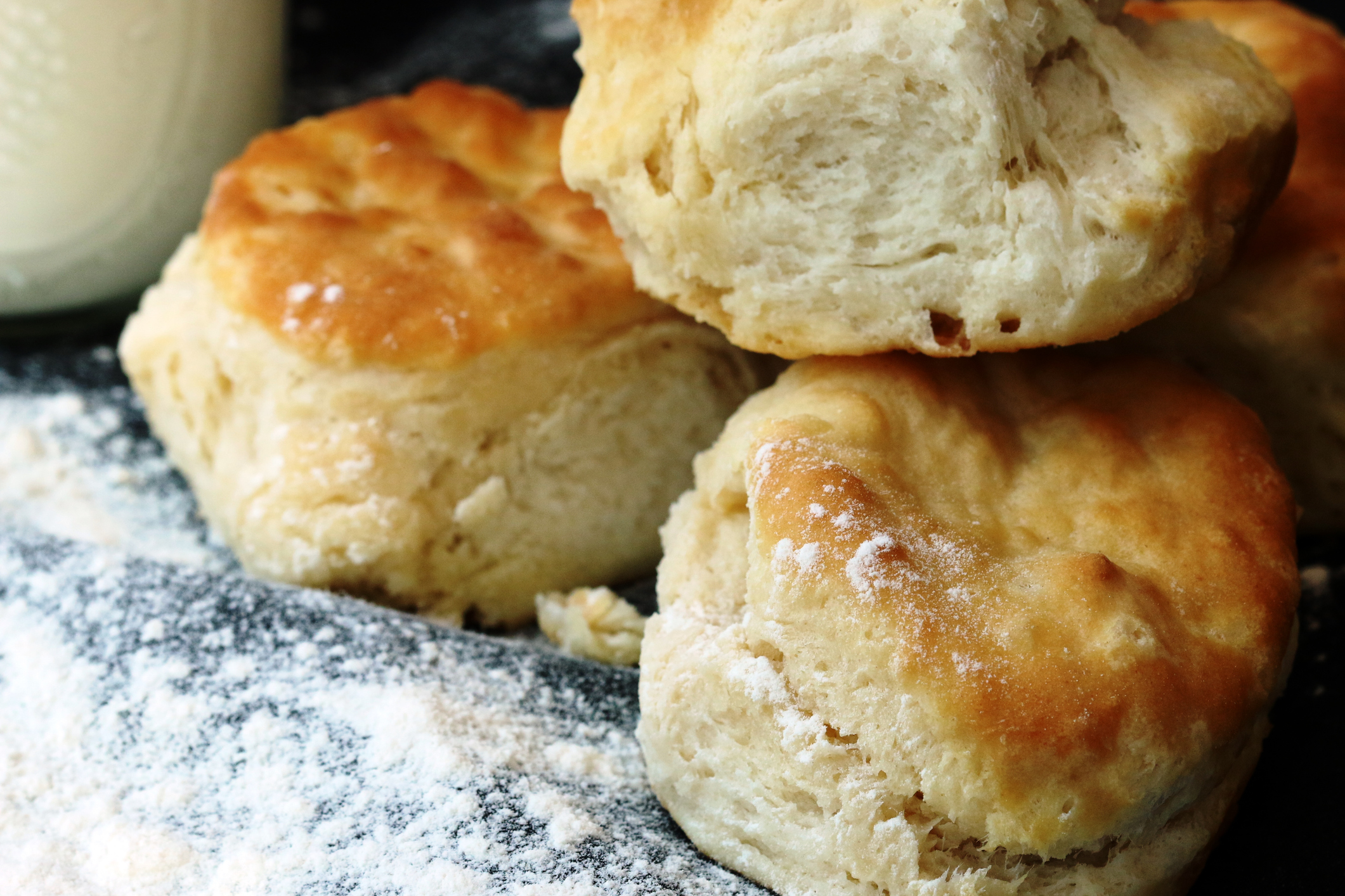 Three lightly browned sourdough biscuits are piled on a flour-covered surface.