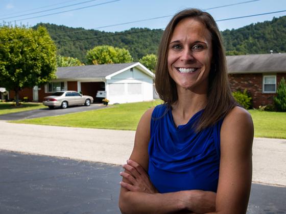 Female researcher standing with arms crossed in front of a house.