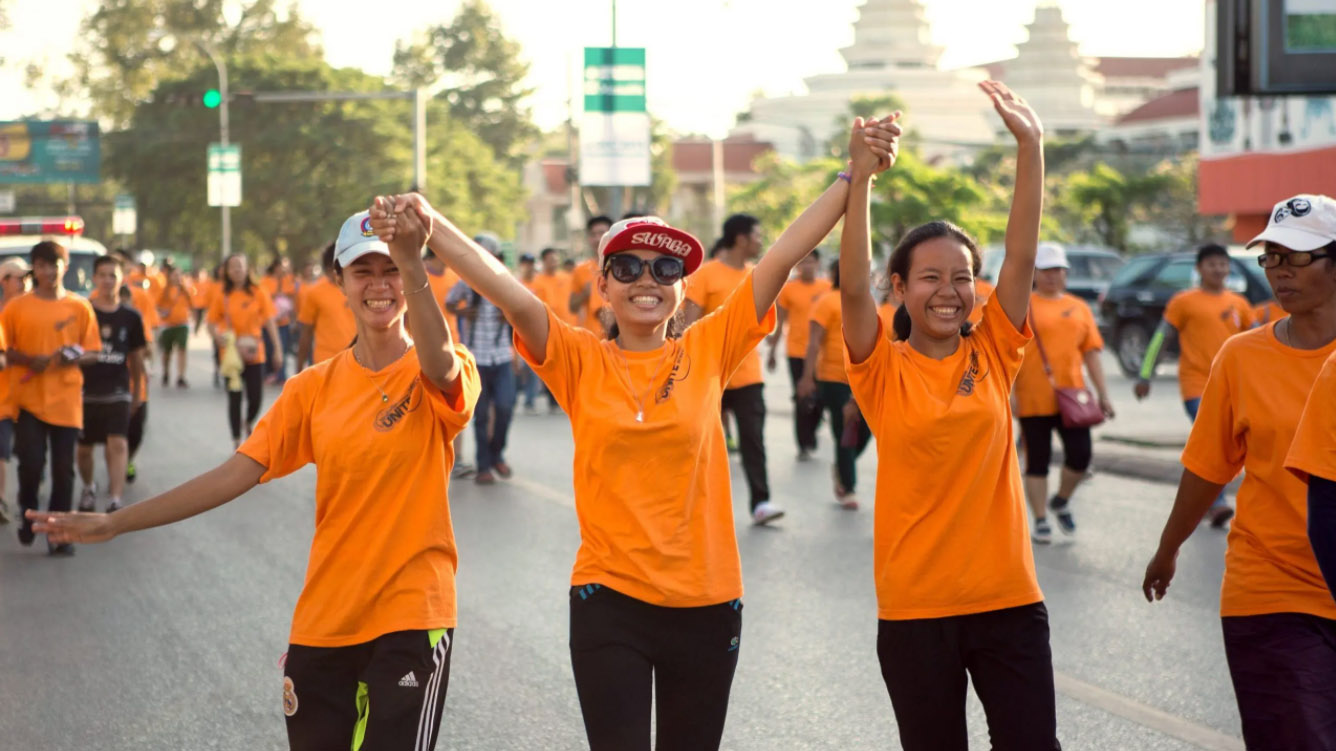 Three girls wearing orange walk among a crowd of people wearing orange. 